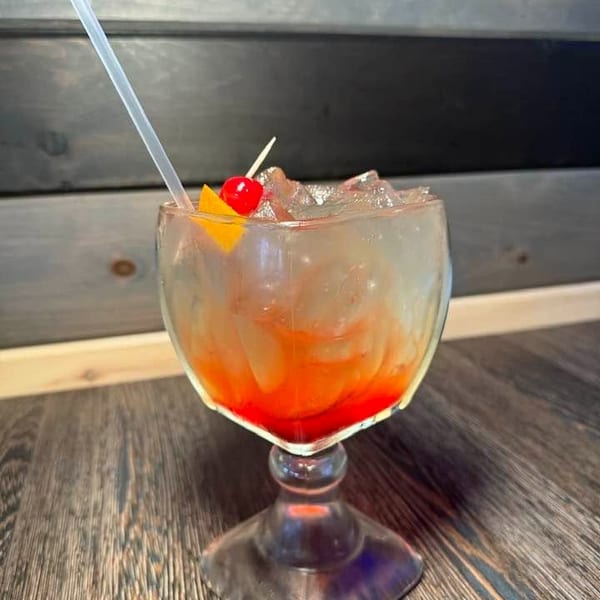 A vibrant red and orange cocktail with ice, a cherry, and an orange slice, on a wooden table.