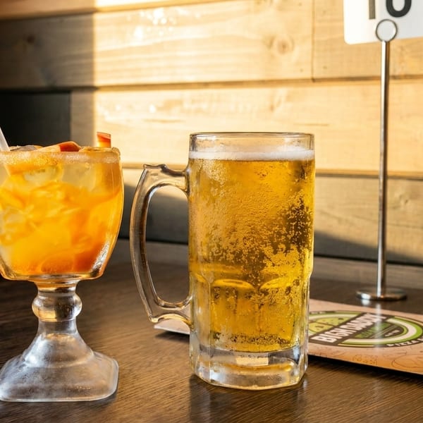 A refreshing cocktail with fruit and a frosty beer mug on a wooden table.