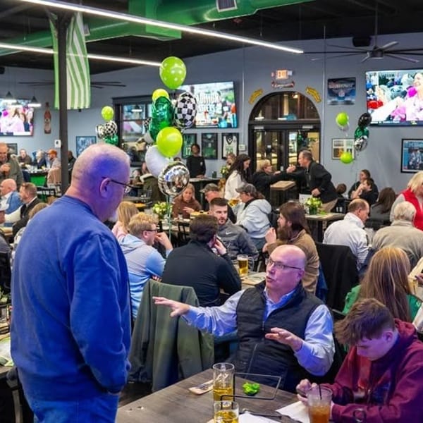 A lively restaurant interior filled with many people dining and socializing, decorated with green and white balloons.