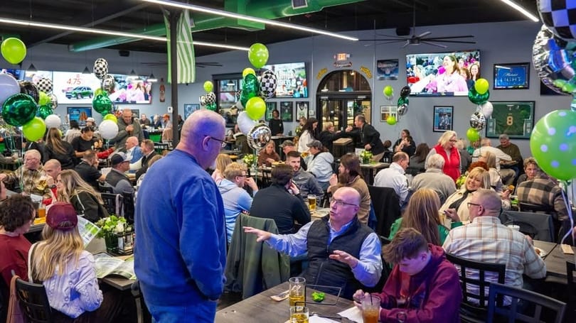 A lively restaurant interior filled with many people dining and socializing, decorated with green and white balloons.