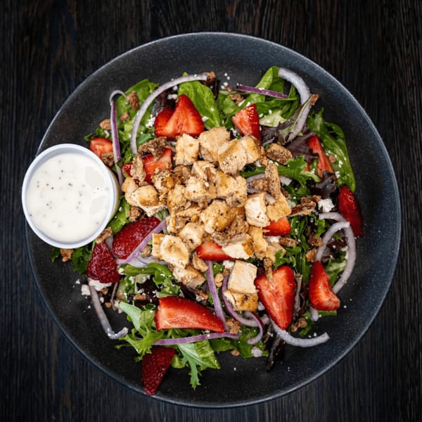 Overhead view of a salad with chicken, strawberries, red onion, and dressing on a dark plate.