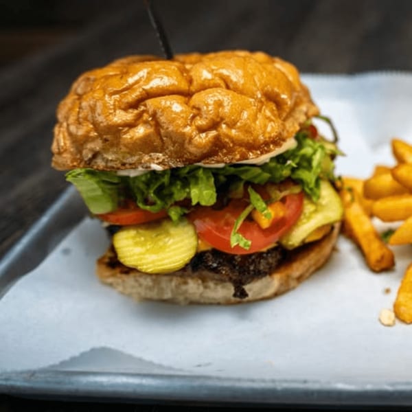 Juicy burger with lettuce, tomato, pickles, and fries on a metal tray.